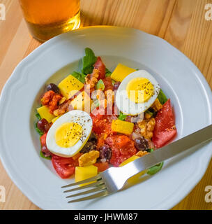 Dinner salad, with hard-boiled egg, tomatoes, cheddar chess, olives, walnuts, salsa fresca, baby arugula, and a cool pint of larger beer Stock Photo