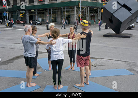 At the conclusion of an outdoor free yoga class the instructor (maroon top) leads the group in a moment of thought & prayer. On Astor Place in NYC Stock Photo
