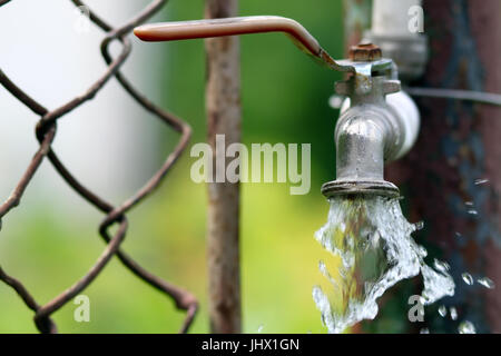 Close up of grunge brass faucet on green bokeh background. Water shortage and earth day concept. Stock Photo