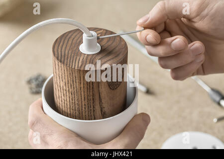 Working process in the workshop. Man is using a wrench when putting a bushing into the part of the lamp. He is fixing the electric cable. Closeup. Hor Stock Photo