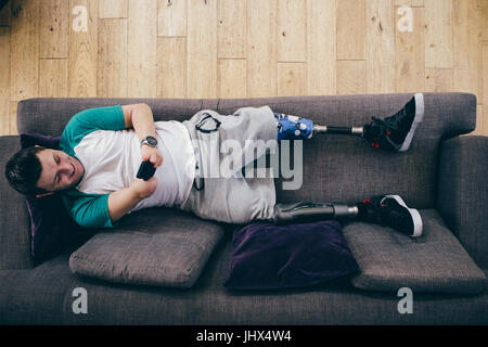 Quadriplegic man lying on the sofa at home. He is using a smartphone. Stock Photo