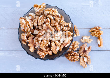 Many walnut kernels in a glass bowl on a wooden background of a gray-blue color. Stock Photo