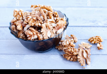 Many walnut kernels in a glass bowl on a wooden background of a gray-blue color. Stock Photo
