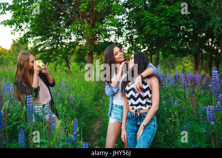 Three hipsters girls blonde and brunette taking self portrait on polaroid camera and smiling outdoor. Girls having fun together in park. Stock Photo