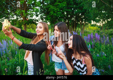 Three hipsters girls blonde and brunette taking self portrait on polaroid camera and smiling outdoor. Girls having fun together in park. Stock Photo