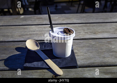 Small white disposable coffee cup with straw and chocolate placed on napking on rustic wooden table with disposable spoon. Stock Photo