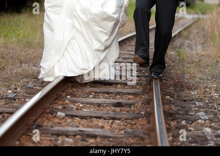 Bride and groom run on rail in the railway station - bridal couple At a railway station, walking on straight, Brautpaar laufen auf Schiene am Bahnhof  Stock Photo