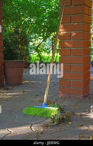 A green broom with rusty handle lean on the brick pillar Stock Photo