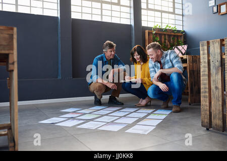 Three colleagues discussing paperwork layed out on an office floor Stock Photo