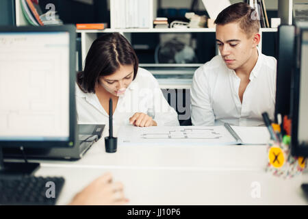 Couple of young designers working at modern office, two coworkers discussing fun project over a laptop, little team of businesspeople smiling and look Stock Photo