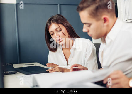 Couple of young designers working at modern office, two coworkers discussing fun project over a laptop, little team of businesspeople smiling and look Stock Photo