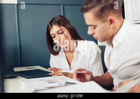 Couple of young designers working at modern office, two coworkers discussing fun project over a laptop, little team of businesspeople smiling and look Stock Photo