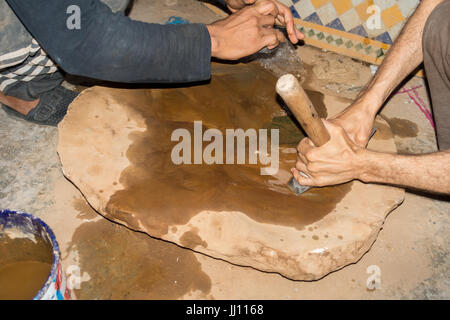 Moroccan craftsmen are sharpening their hammers on a wet stone on the floor. Stock Photo