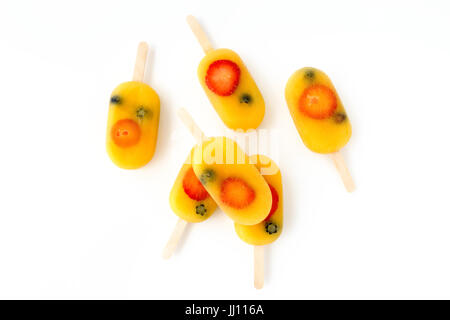 Homemade fruit ice pop, popsicle, ice cream lolly with orange juice, fresh strawberries and blueberries arranged on a white background with copy space Stock Photo