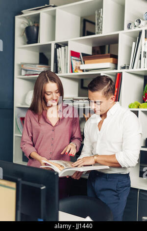 Two male international students reading book about marketing together preparing for test sitting in library while joking and having fun. Creative blog Stock Photo