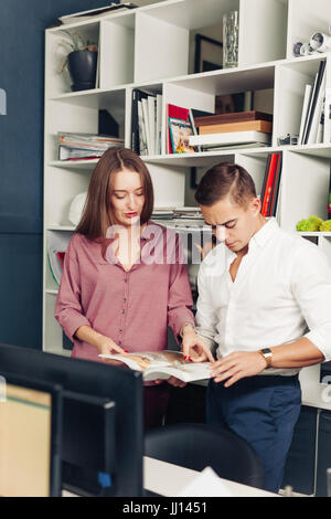 Two male international students reading book about marketing together preparing for test sitting in library while joking and having fun. Creative blog Stock Photo