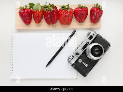 Notebook mock up for artwork with old camera, pen and red strawberries. Top view. Place for text. Stock Photo