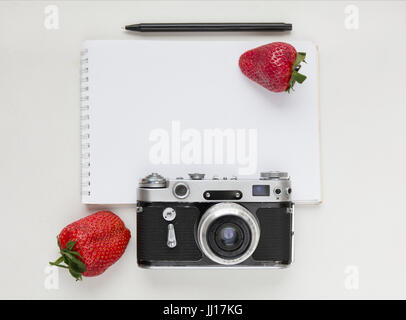 Notebook mock up for artwork with old camera, pen and red strawberries. Top view. Place for text. Stock Photo