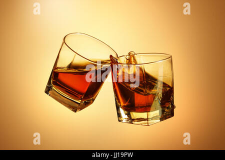 Two whiskey glasses clinking together on brown Stock Photo