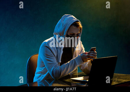 Hooded computer hacker stealing information with laptop Stock Photo