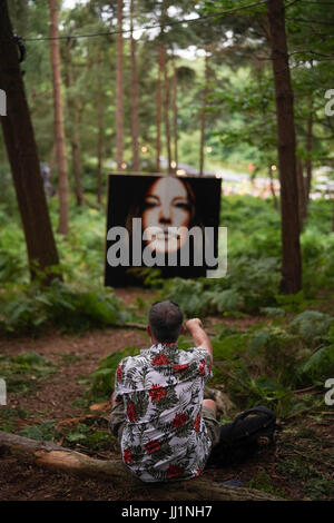 A man throws a stone towards a painting in the woods on day 4 of the 2017 Latitude festival in Henham Park, Southwold in Suffolk. Photo date: Sunday,  Stock Photo