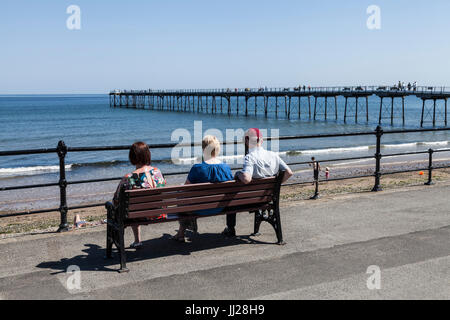 Three people sat on a bench looking out to sea at Saltburn by the Sea,England,UK Stock Photo