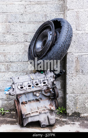 Old engine and car wheel with tyre dumped against an old breeze block wall. Stock Photo
