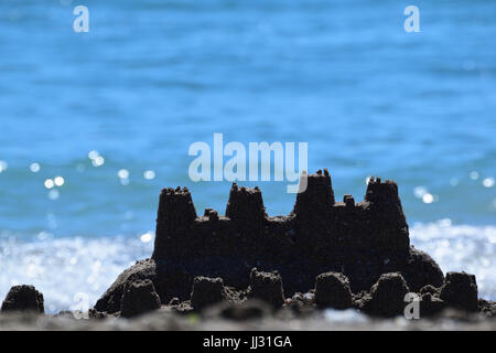 A little beach sandcastle built on the shore of the Black Sea made of fine sand and decorated with some seashells. Blue Sea waves in the backgground. Stock Photo