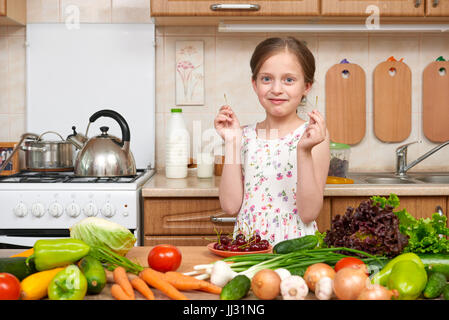 child girl eat cherries, fruits and vegetables in home kitchen interior, healthy food concept Stock Photo