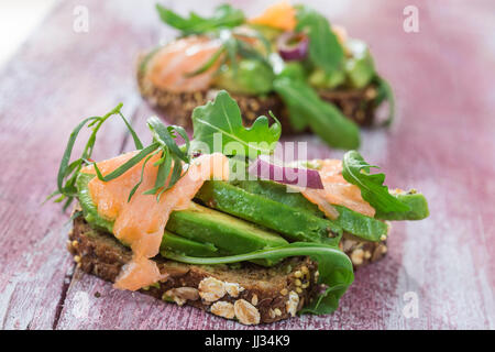 Countrybread Avocado, salted salmon sandwich with fresh herbs on pink craked paintt wooden board background. Healthy eating theme Stock Photo