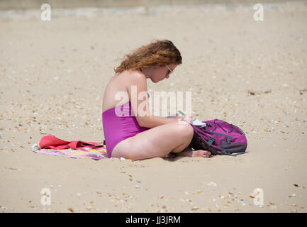 Young woman sitting on a beach in hot weather working, making notes, Bournemouth, Dorset, UK, 18th July 2017.