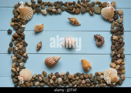 full large decorative frame from pebbles stones rocks and different seashells on light blue surface wooden desk. great as background for summer vacati Stock Photo