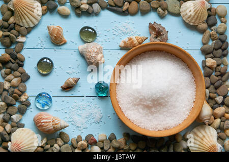 large decorative frame from pebbles stones rocks and different seashells on light blue surface wooden desk. large bowl with sea salt on wooden planks  Stock Photo