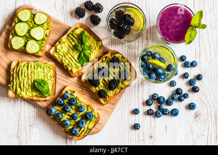 Set of vegetarian toast sandwiches with avocado and drinks. Variety of healthy food and drinks on white wooden background. Stock Photo