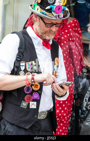 Traditional English folk dancer, mature male Morris man with beard, standing in the street and looking down at his mobile phone while texting. Stock Photo