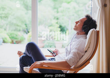 listening relaxing music at home, relaxed man in headphones sitting in deck chair in modern bright interior Stock Photo