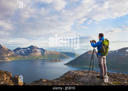 landscape photographer working with tripod and dslr camera in beautiful wild nature, standing with backpack on top of mountain Stock Photo