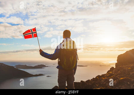 hiking in Norway, silhouette of tourist with norwegian flag looking at beautiful fjord nature with light of midnight sun Stock Photo
