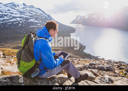 man tourist backpacker using internet application on tablet computer outside in mountains Stock Photo