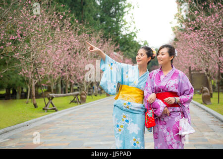 Happy friends looking at view and pointing of sakura park. Smiling asian women enjoying with blossom cherry-blossom. Stylish young japanese girls in k Stock Photo