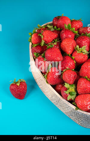 ripe strawberries in heart shaped wooden dish on turquoise painted wood Stock Photo