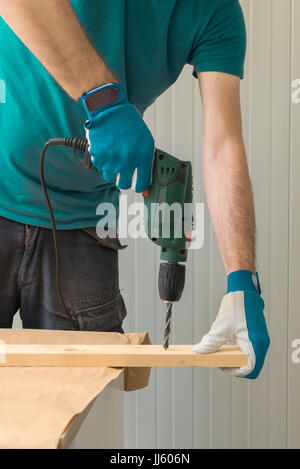 Carpenter handyman using electric drill to make holes on plank on the woodwork workshop table Stock Photo