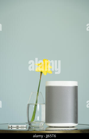 Wireless speaker and mobile phone on a mirrored table with a yellow daffodil. Stock Photo