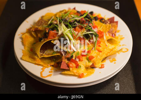 Plate of nachos with melted cheese, black olives, green onions, red peppers, green peppers and tomatoes on room service tray Stock Photo