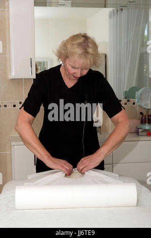 Masseuse preparing the client bed with a paper roll Stock Photo
