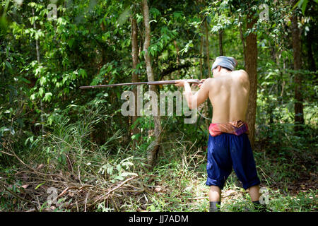 Asian man farmer aiming gun a rifle walks along in the forest background. Hunting and the way of life of rural people in Thailand concept. Stock Photo