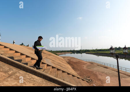 Asian young man engineers are holding a blueprint. While walking down the stairs to the floodgates for check progress of the  construction project. In Stock Photo