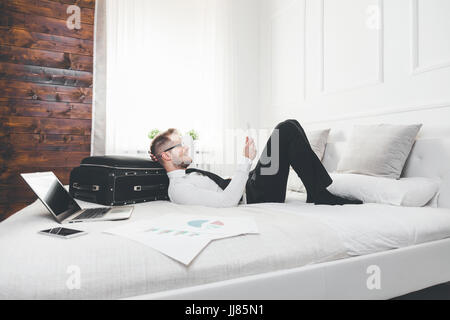 Young businessman on bed working with a tablet laptop from his hotel room Stock Photo
