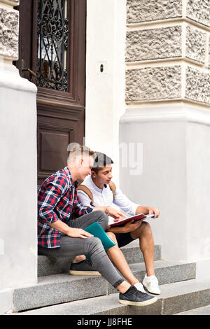 Teenage students sitting on stone steps in front of university. Stock Photo