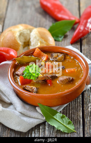 Hot Hungarian goulash soup served in a ceramic bowl with a fresh roll Stock Photo